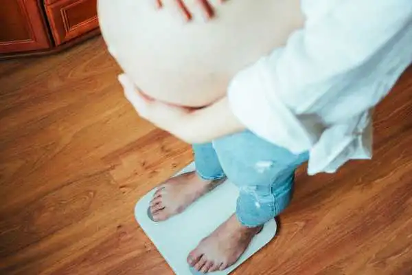Image of woman weighing herself and experiencing weight gain through pregnancy Anniesland